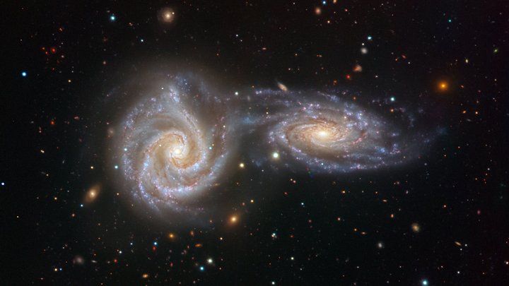 Zwei Spiralgalaxien, aufgenommen mit dem VIMOS-Instruments am VLT | Bildquelle: ESO/Juan Carlos Muñoz Das Bild zeigt zwei spiralfrömige Strukturen und viele helle Punkte